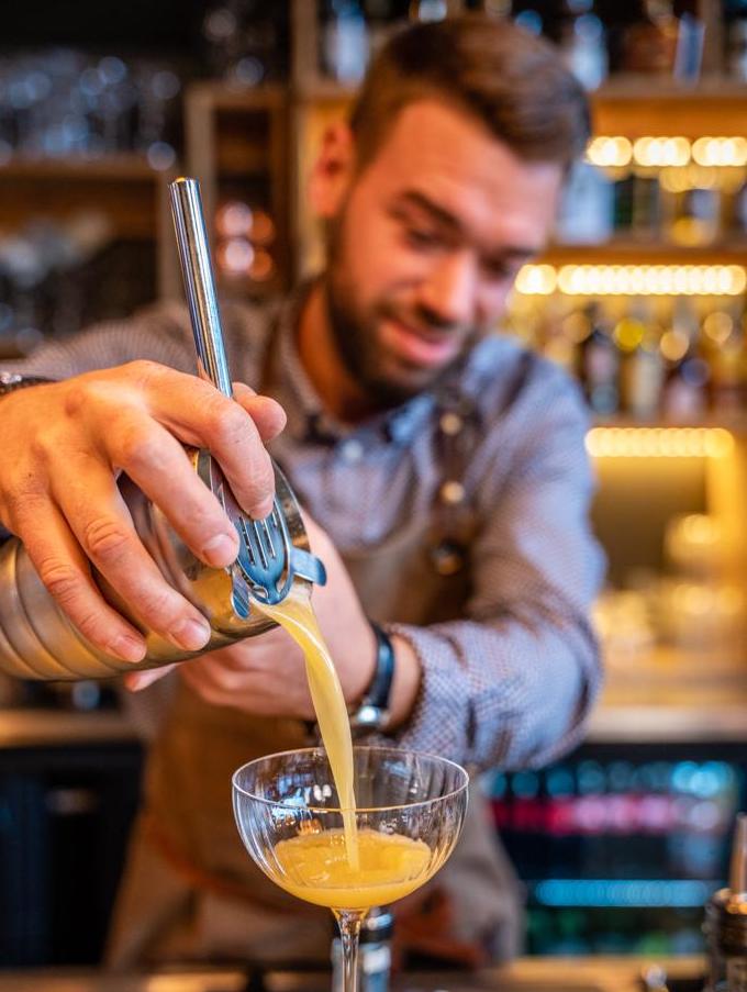 Barman expert préparant un cocktail artisanal coloré, démontrant son savoir-faire et sa créativité dans l'ambiance élégante de notre bar à Serre Chevalier
